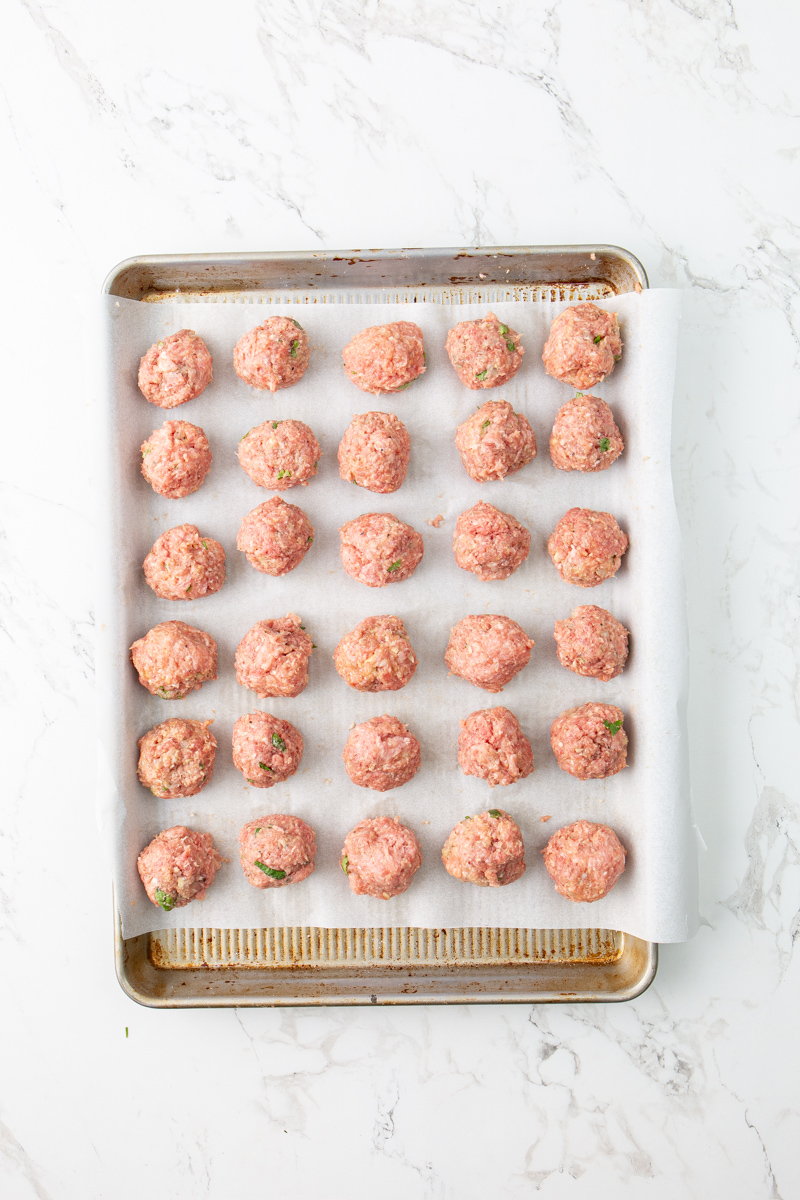 rolled raw meatballs on a parchment lined baking sheet.