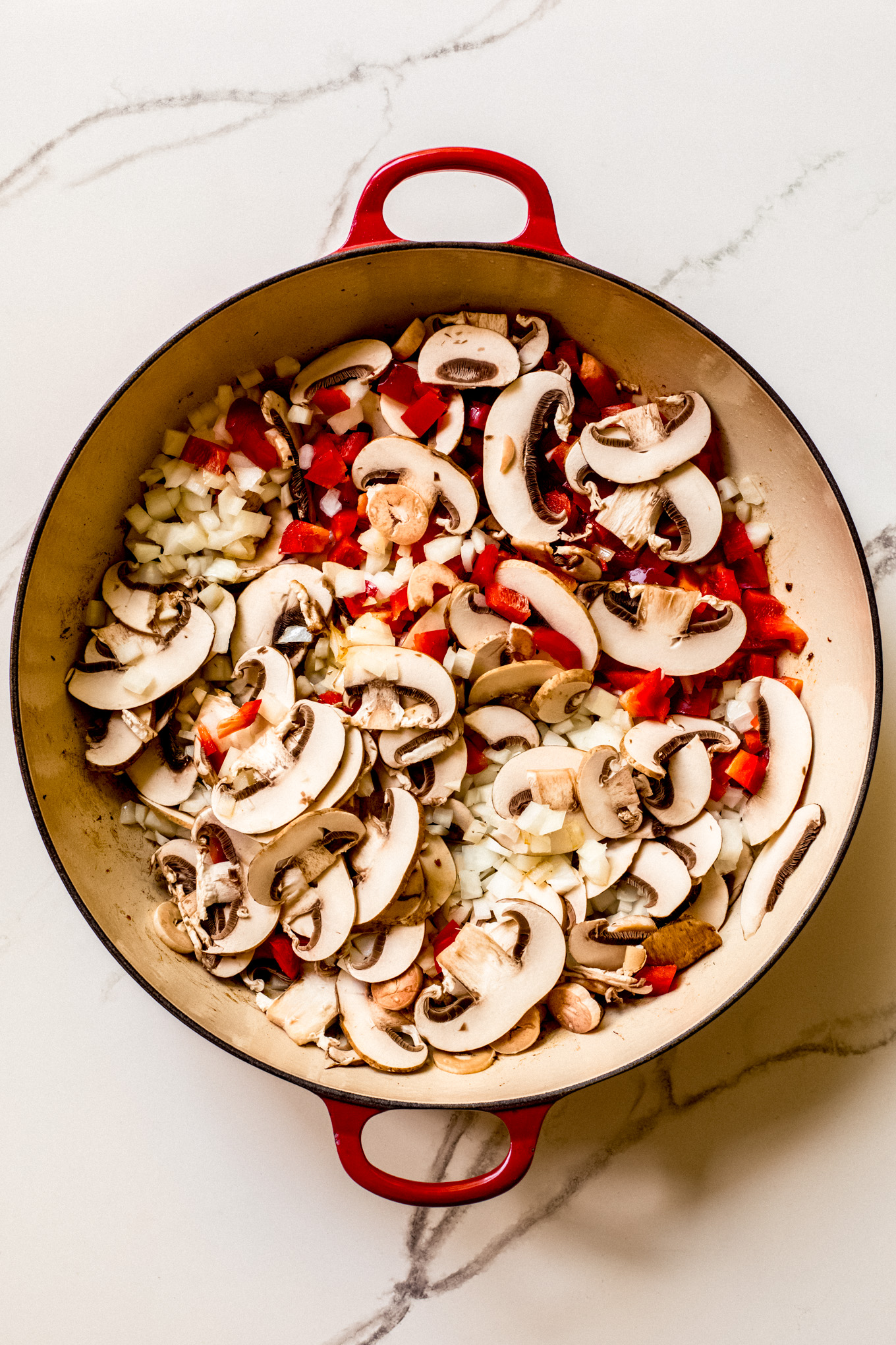 sliced mushrooms, onions, and bell peppers in a saute pan.