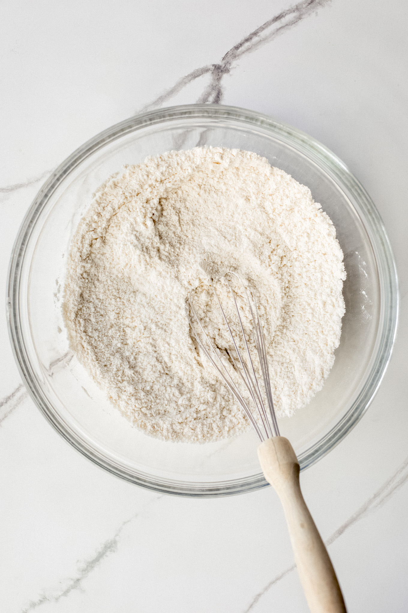 dry cake ingredients with a whisk in a glass bowl.