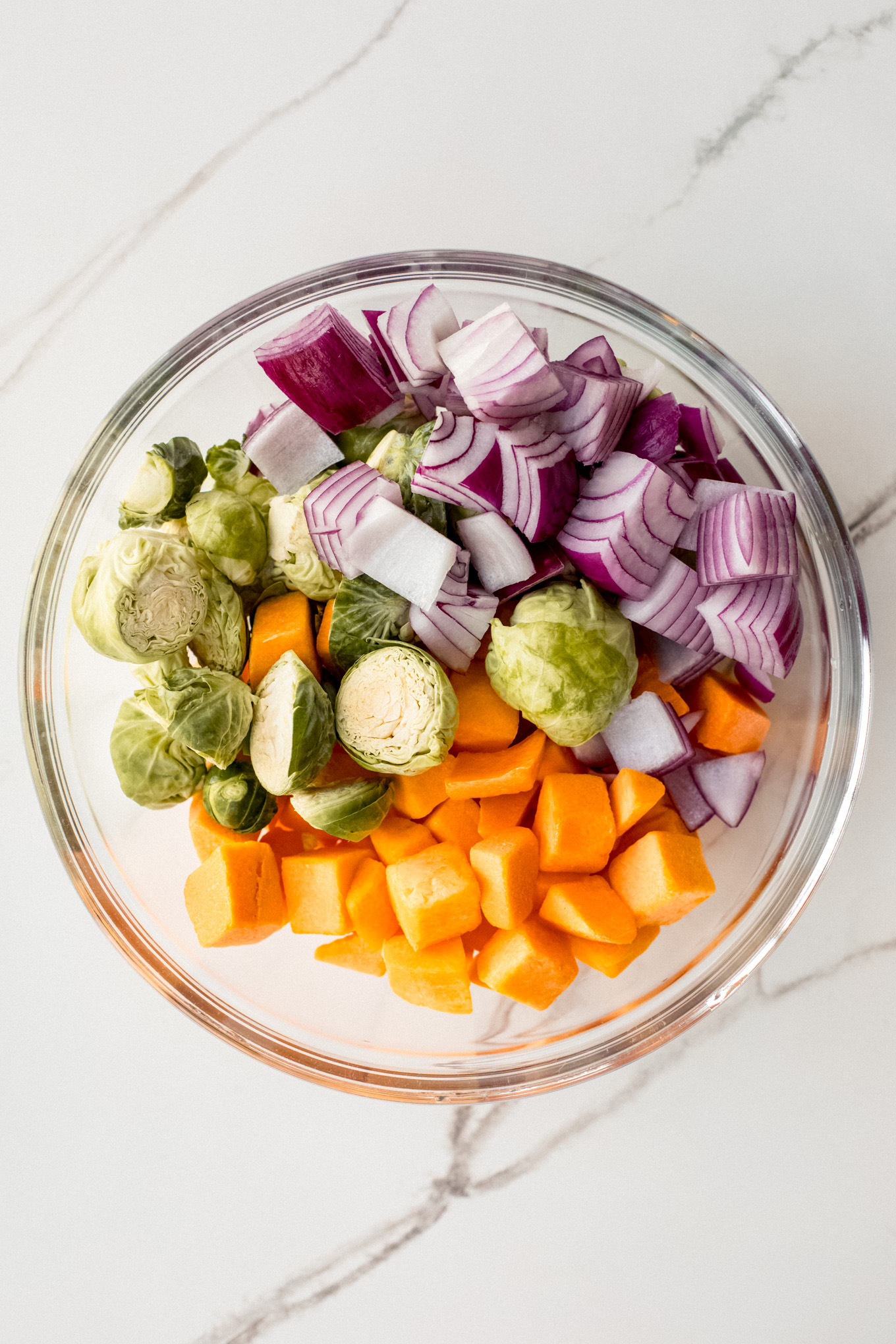 cut up squash, onion, and brussels sprouts in a glass bowl.