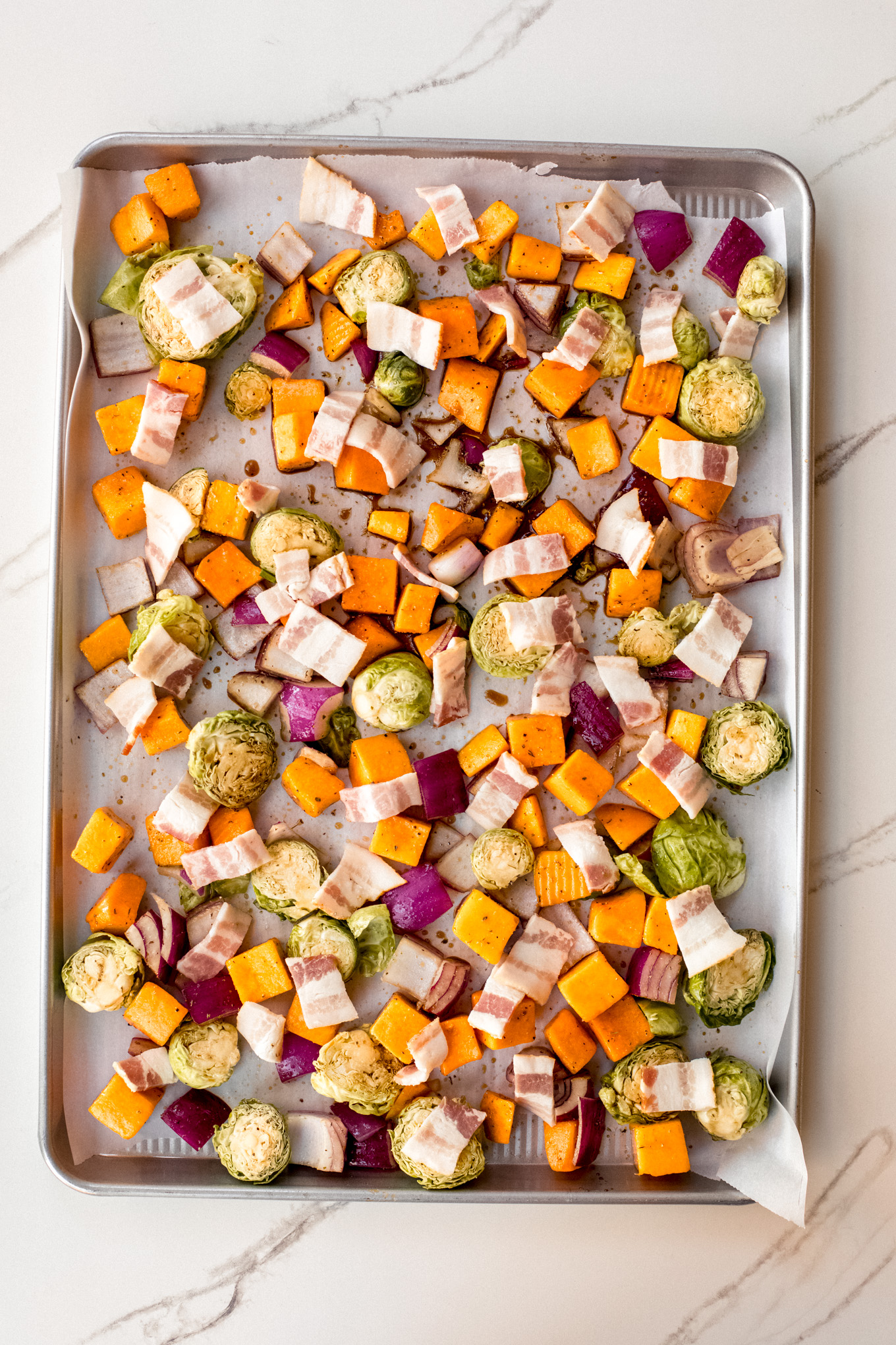 raw cut up vegetables on a sheet pan with bacon.