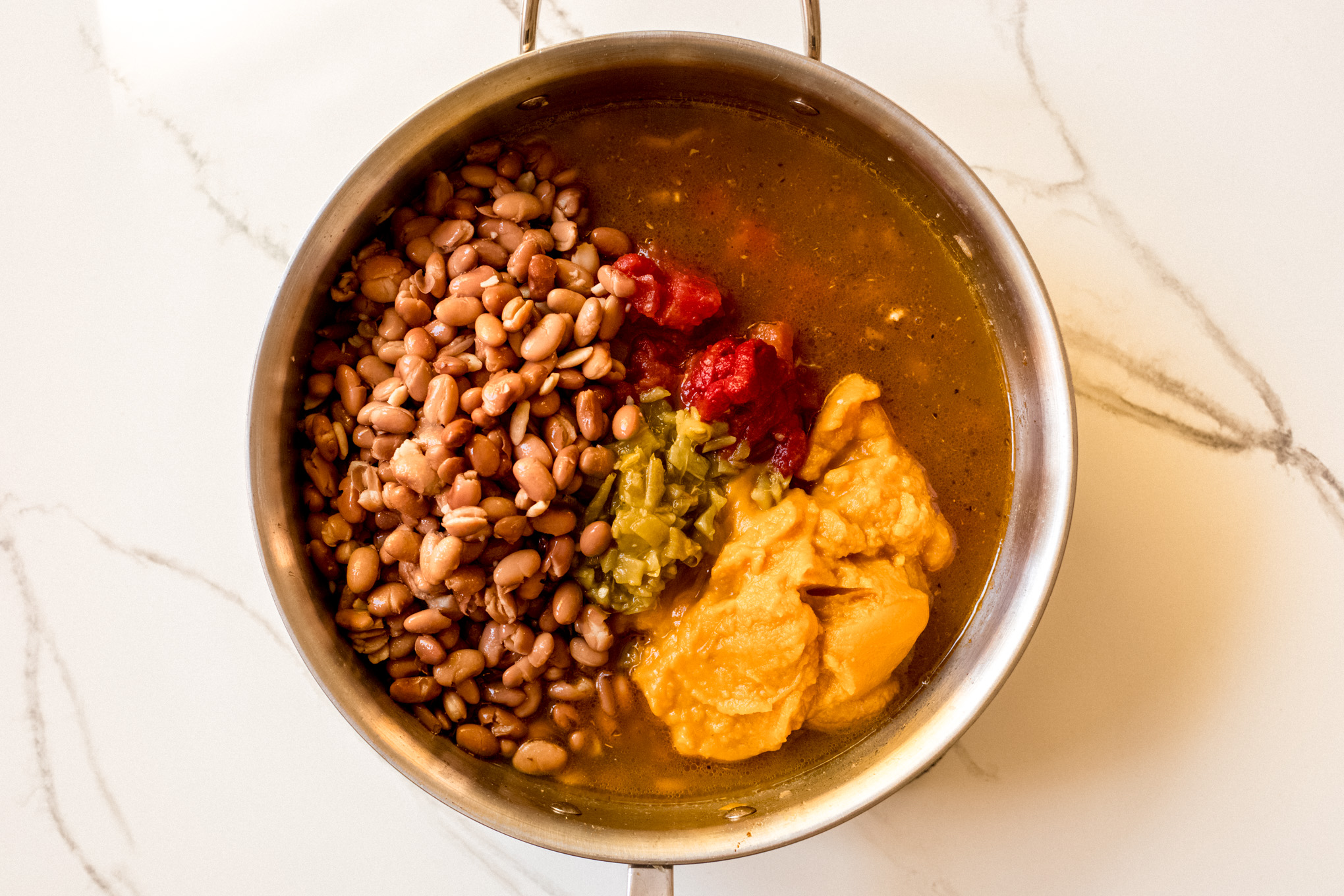 Beans, pumpkin puree, and tomatoes in a pot with cooked turkey.