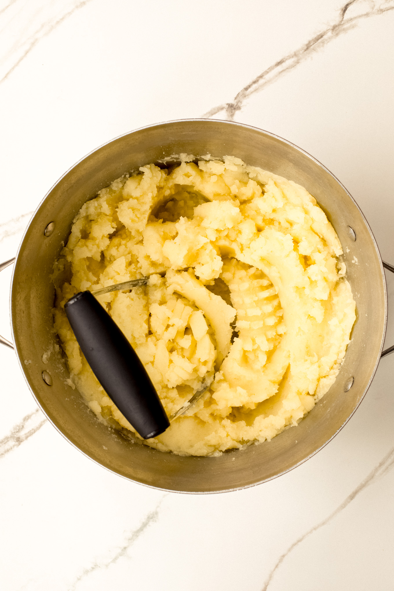 mashed potatoes with a masher in a stockpot.