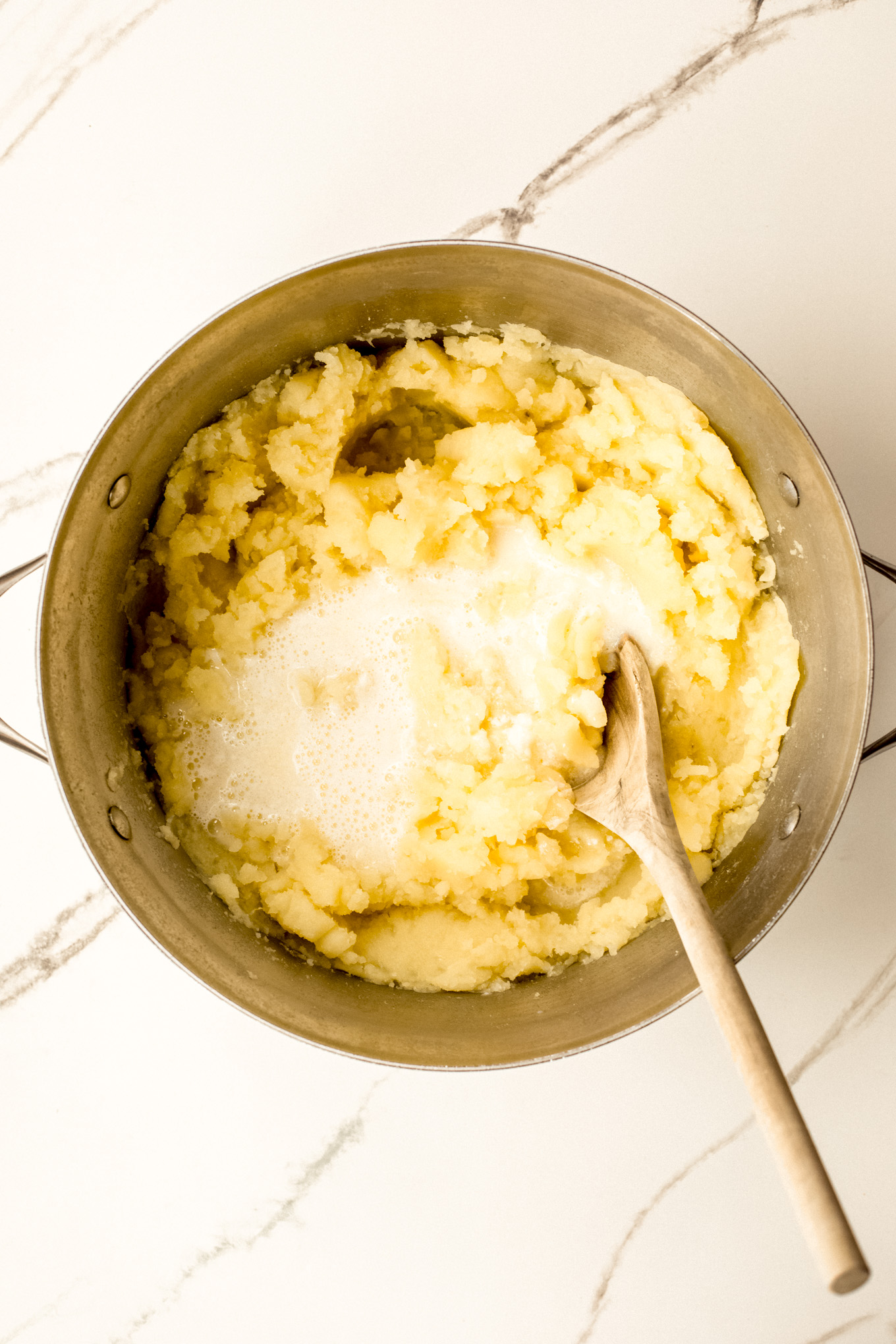 mashed potatoes with milk and wooden spoon.