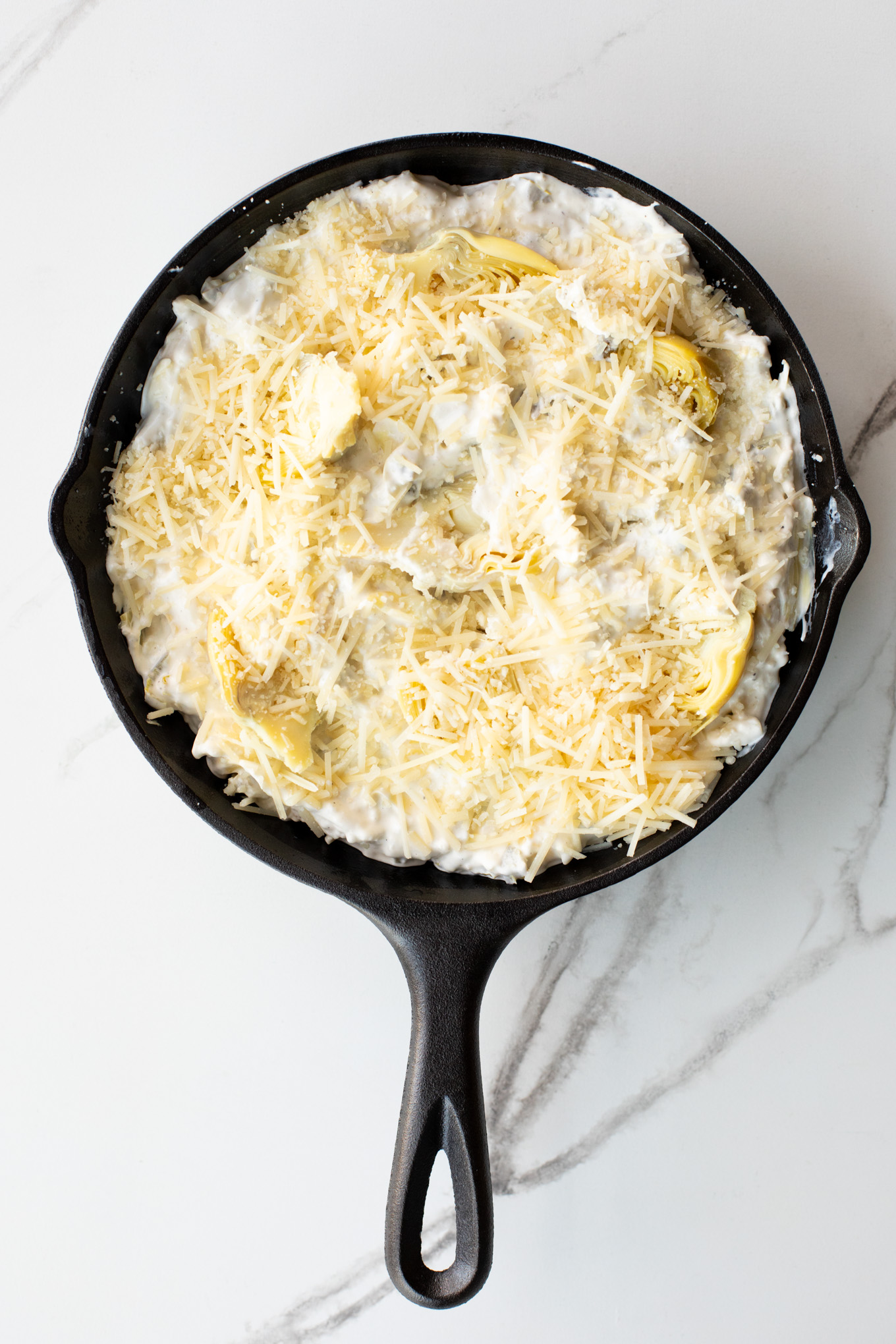 artichoke dip with jalapenos in a cast iron, topped with cheese.