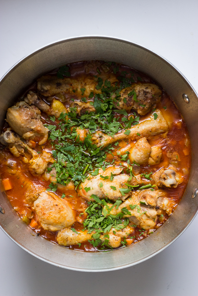 cooked chicken drumsticks and vegetables in sauce garnished with chopped parsley.