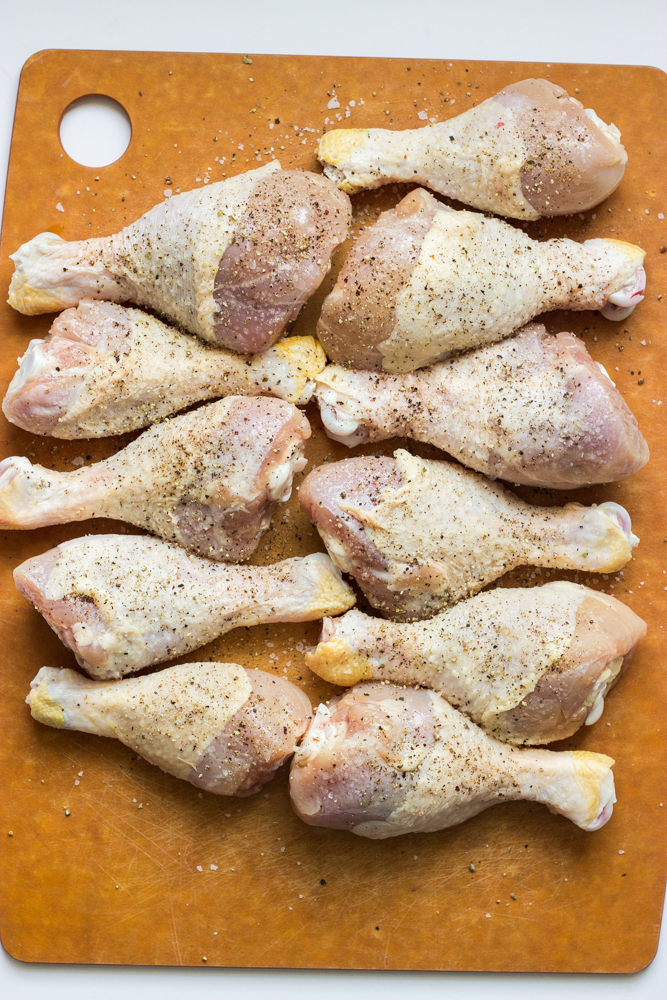 chicken drumsticks on a cutting board seasoned with salt and pepper.