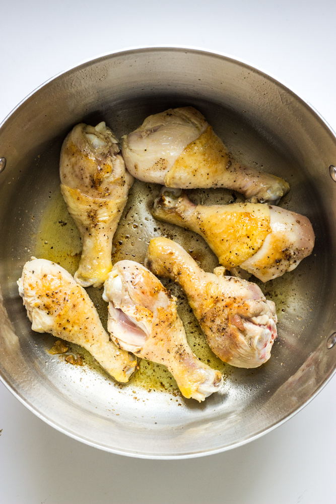 seared chicken drumsticks inside a dutch oven.