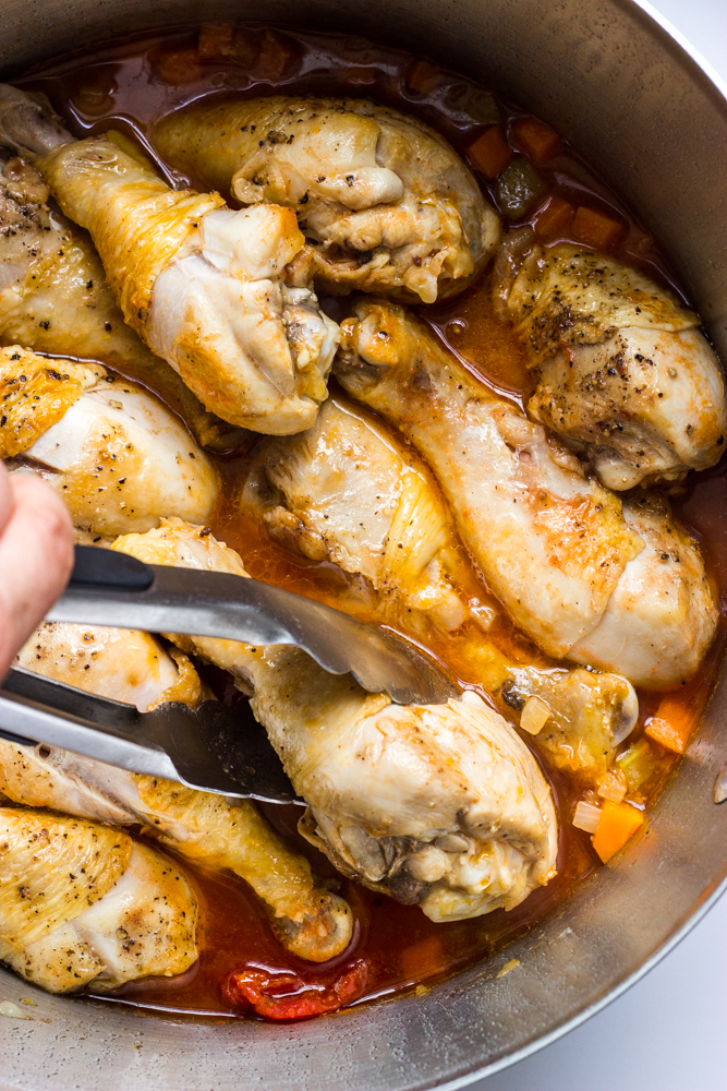chicken drumsticks inside sauce in a dutch oven.