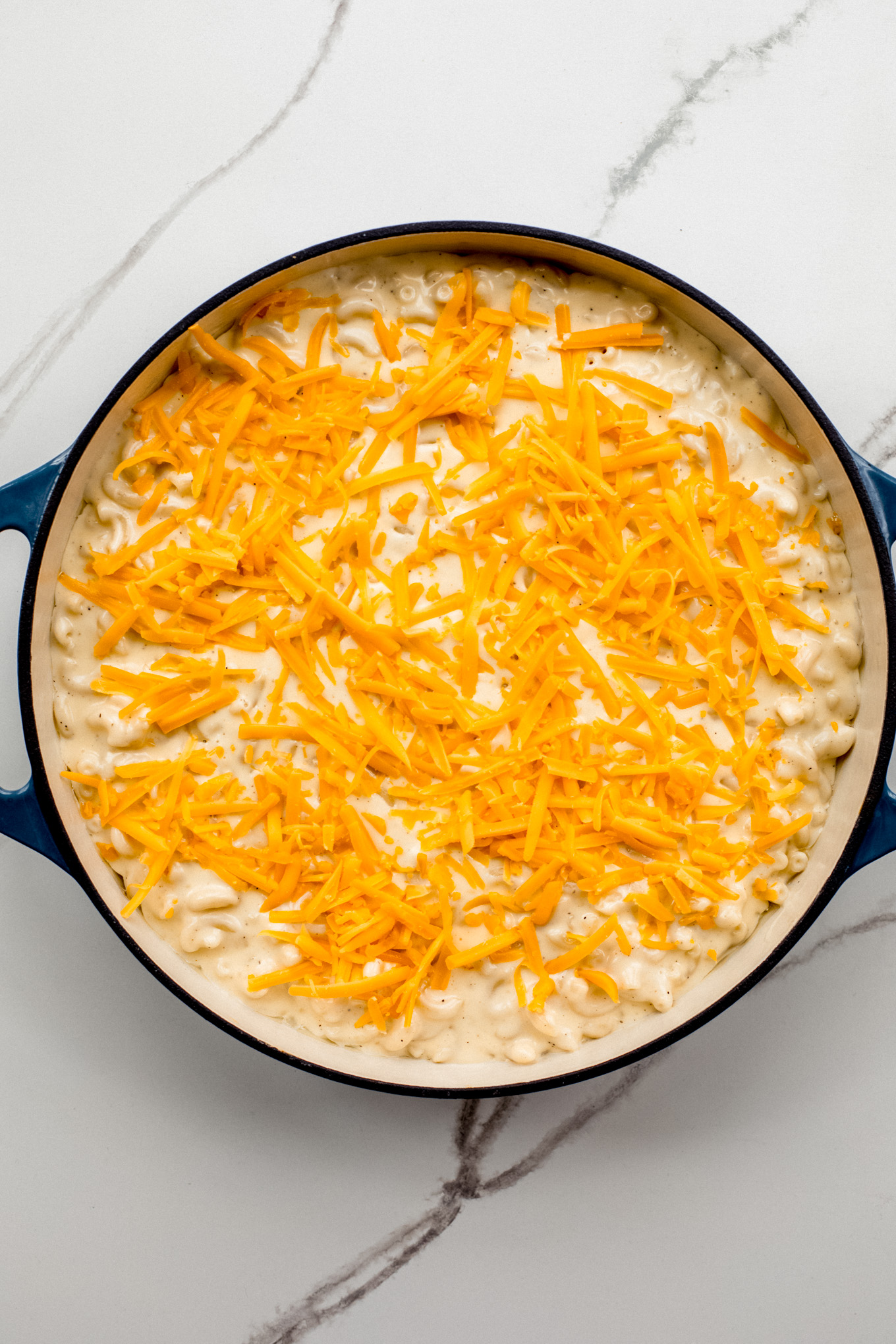baked macaroni in a cast-iron skillet topped with shredded cheddar cheese.