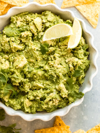 close up of prepared guacamole recipe in a bowl topped with limes.