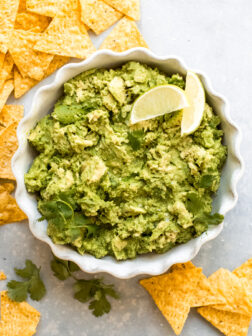 guacamole in a white bowl with a side of tortilla chips.