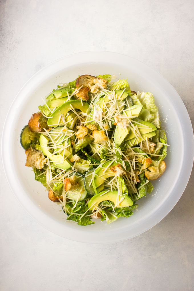 tossed Caesar salad with sliced avocado and Parmesan cheese.