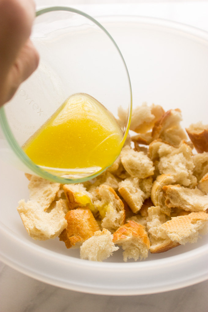 torn pieces of bread in a bowl with melted butter being poured on them.