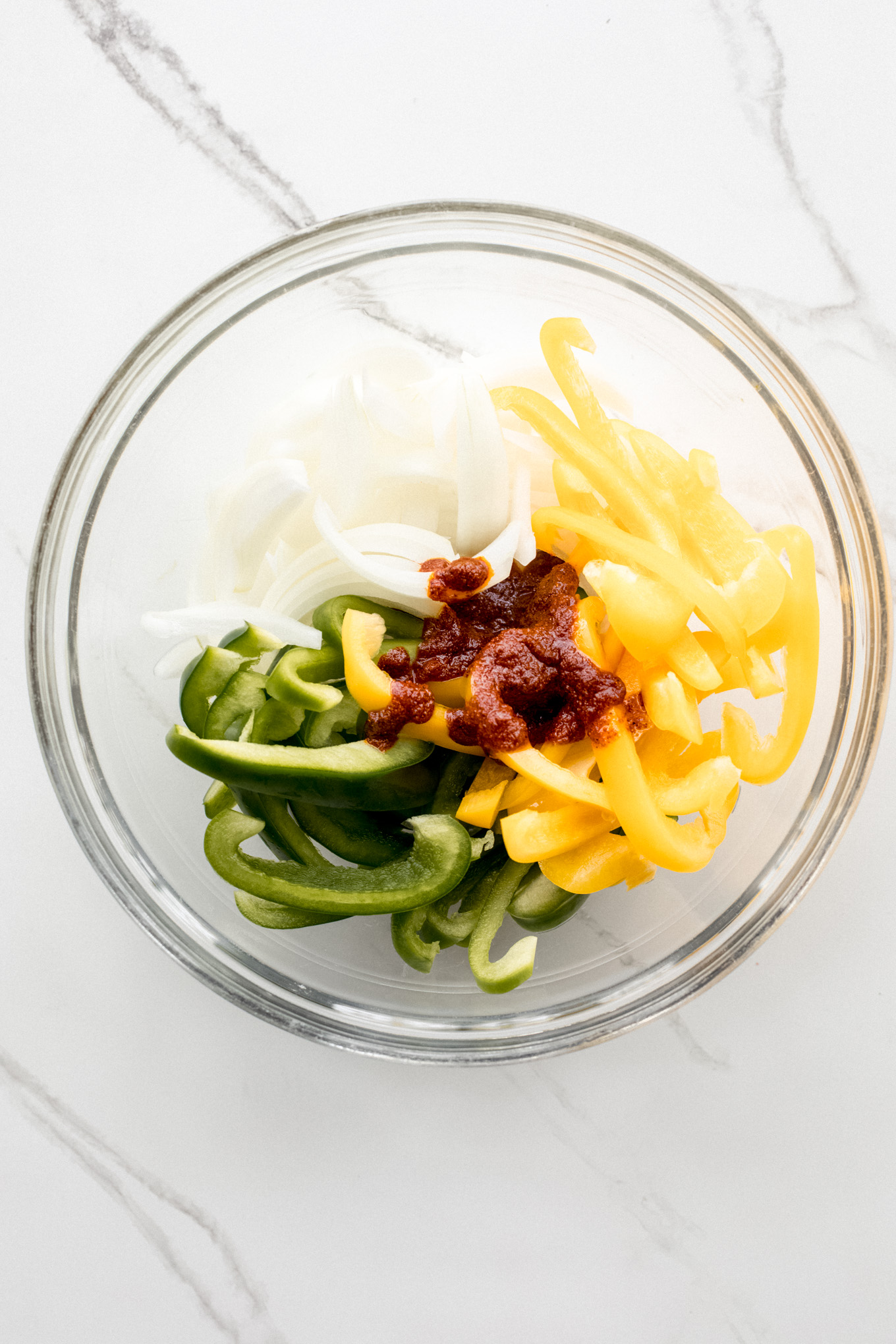 cut up peppers and onions in a glass bowl topped with spice mixture.