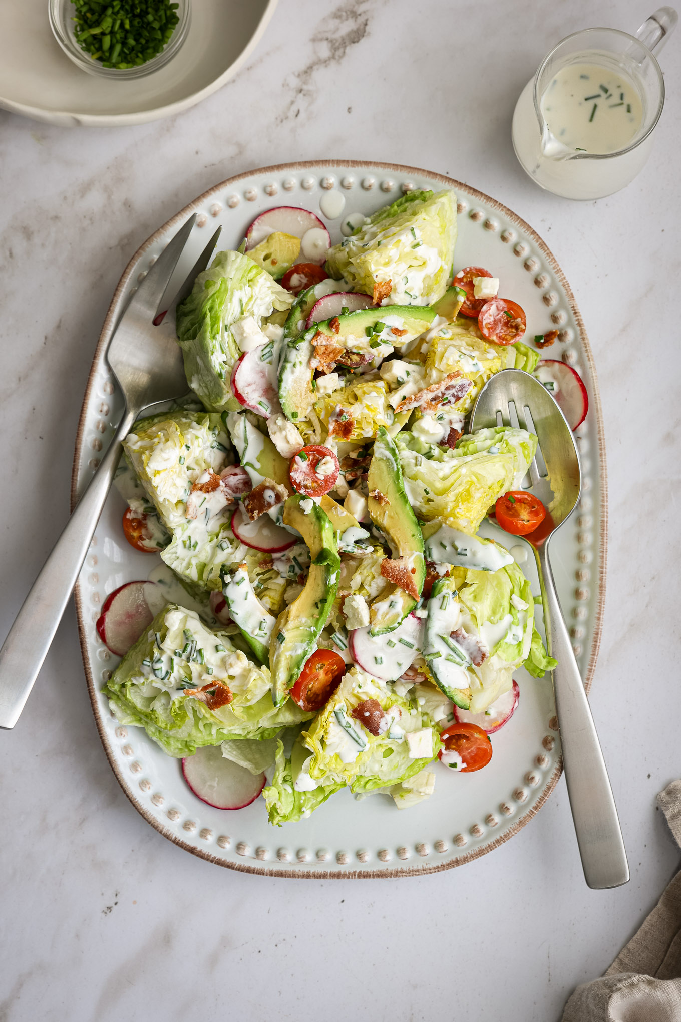 chopped wedge salad on a white platter with avocado, radishes, and tomatoes.