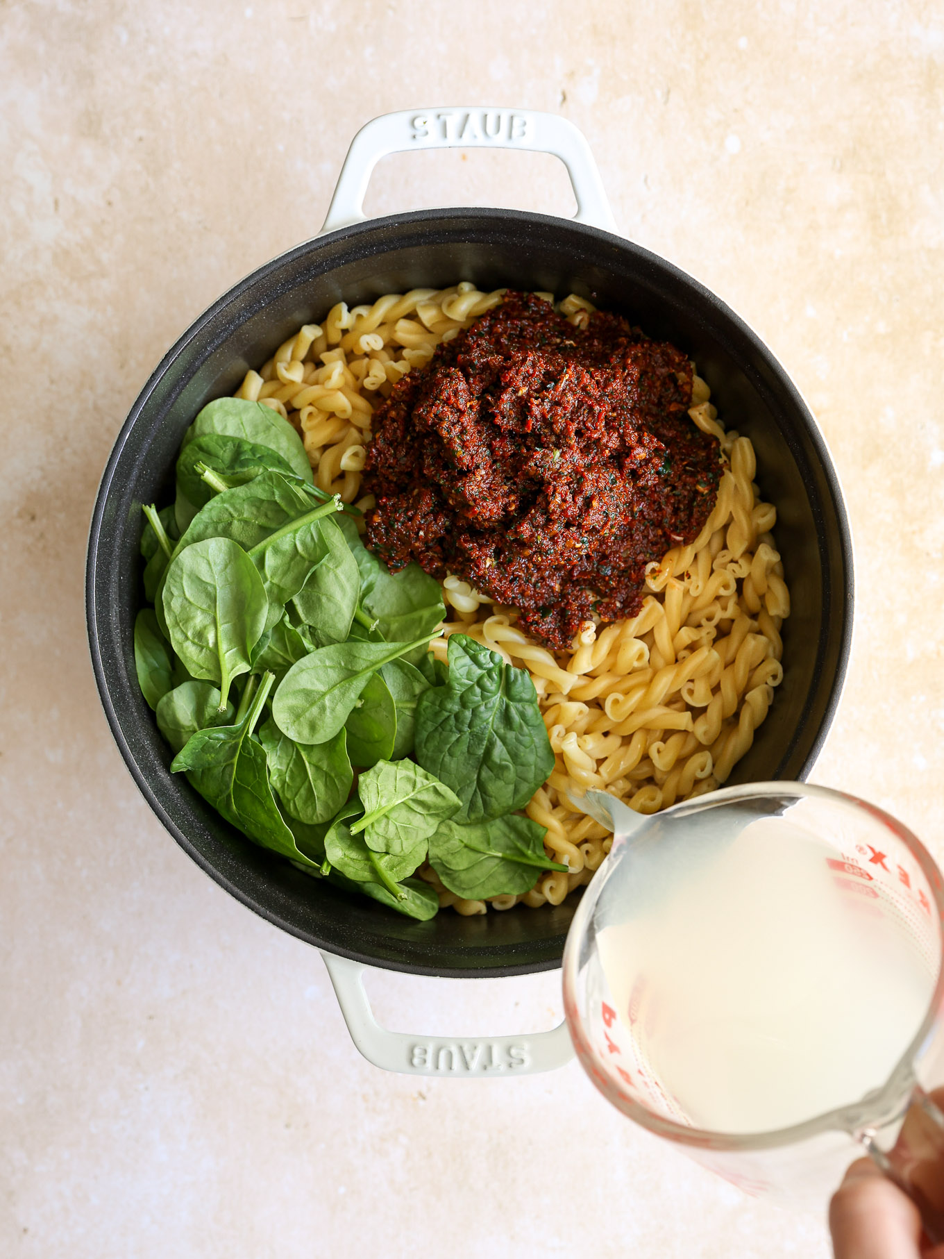 cooked pasta in a pot with spinach and sun dried tomato pesto.