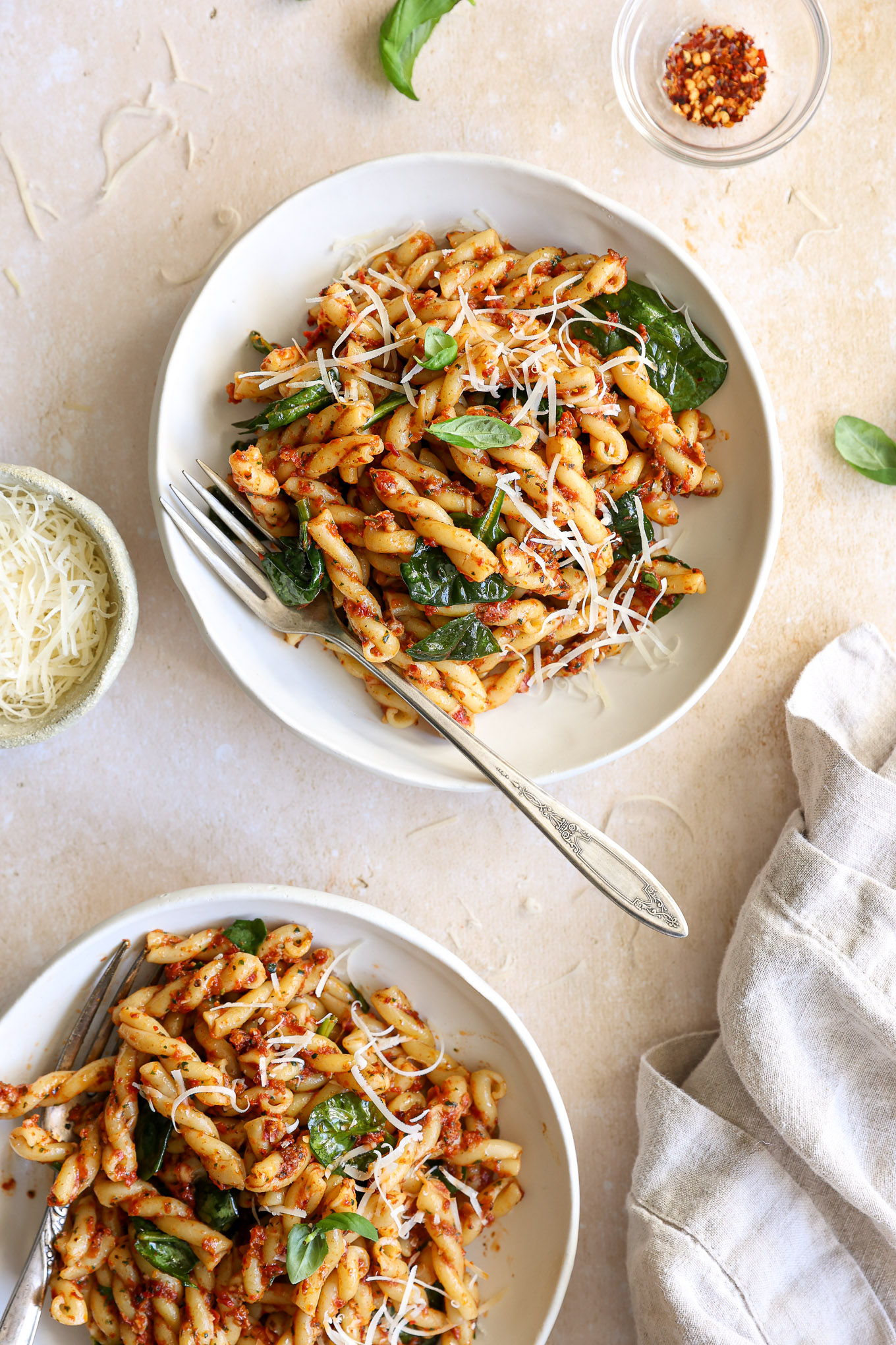 sun-dried tomato pasta with spinach in white bowl with a side of fork.