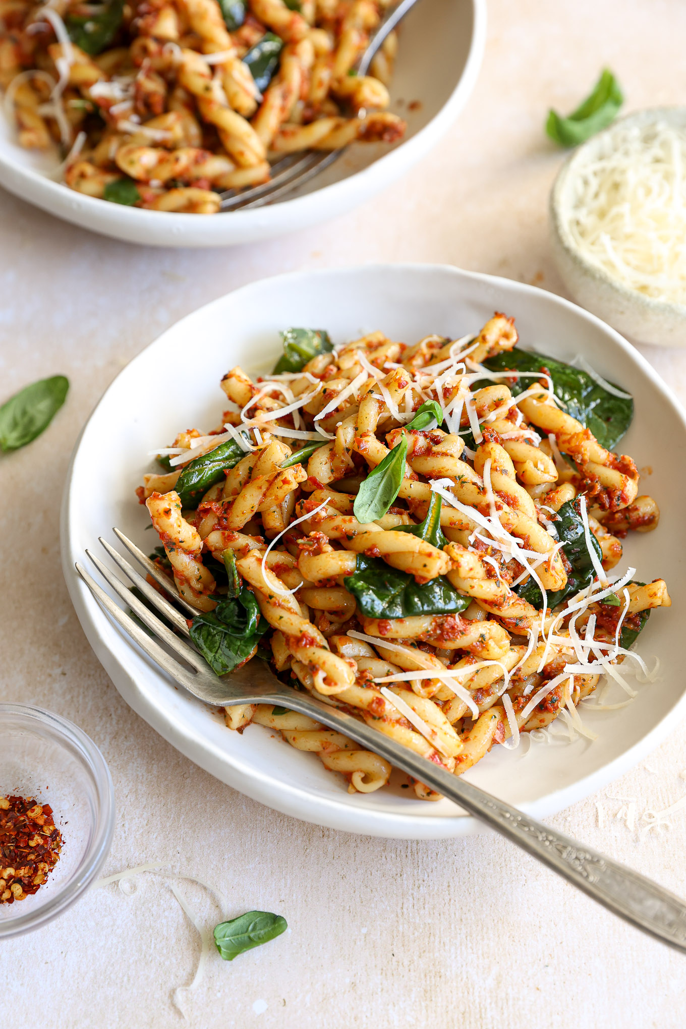 close up of pasta with spinach and sundried tomatoes topped with parmesan cheese.