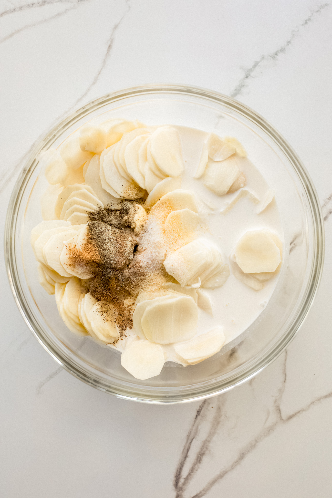 sliced potatoes in a glass bowl with spices.