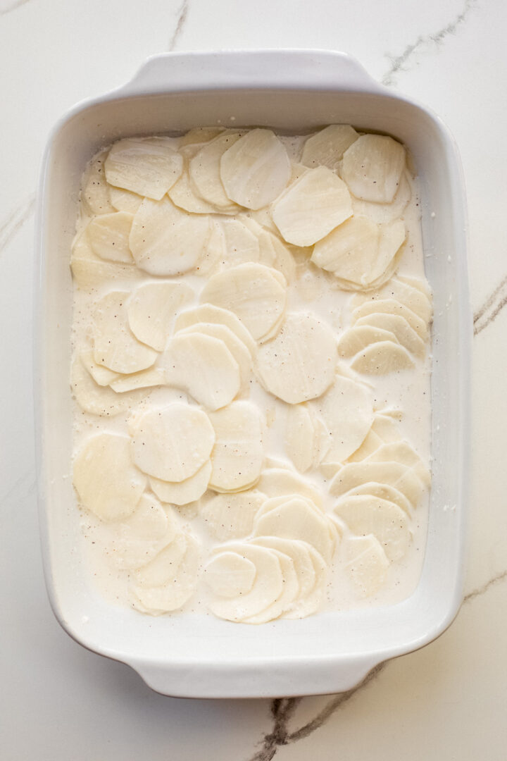 layered sliced potatoes in a white casserole dish.
