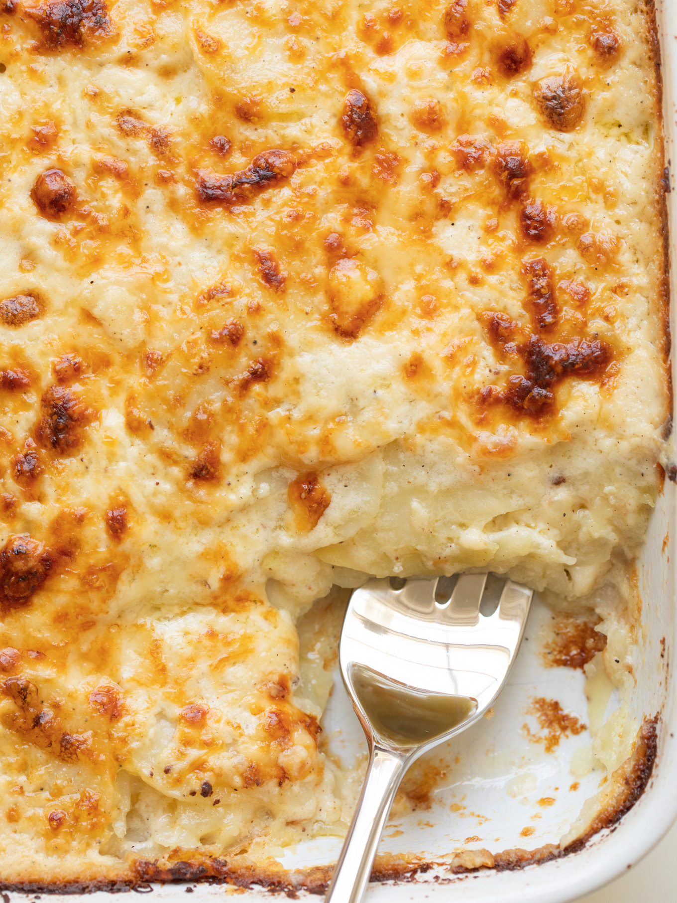 close up scalloped potatoes with cheese in a white casserole.