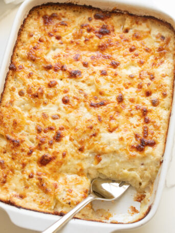 cheesy scalloped potatoes in a white casserole dish with a side of fork.