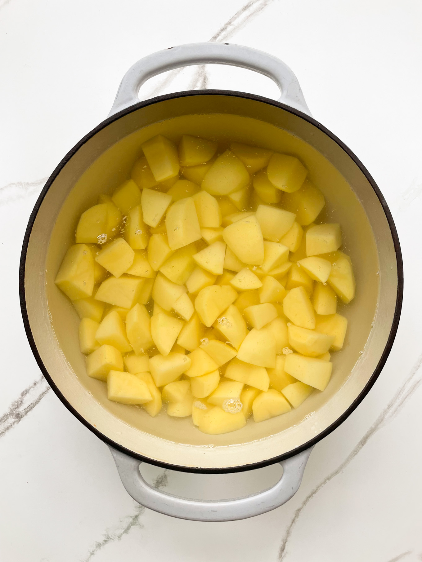 cut up potatoes in a pot with water over them.