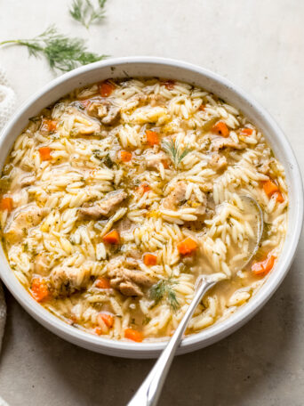side view of chicken orzo soup in a soup bowl with a spoon.