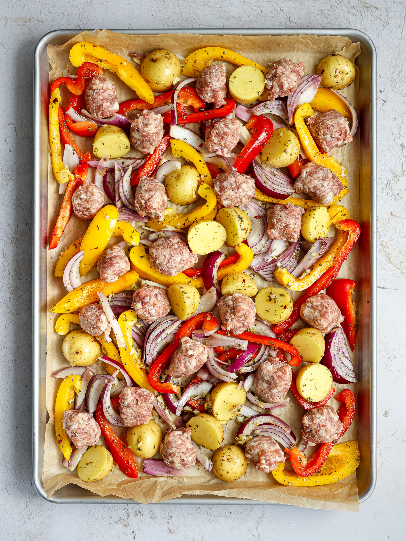 potatoes and raw sausage on a sheet pan.