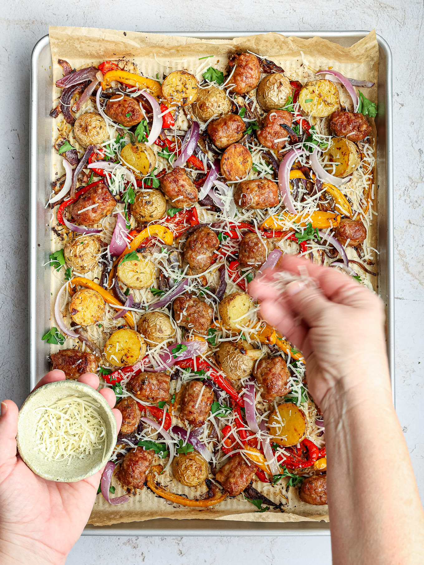 roasted sausage with potatoes on a sheet pan garnished with parmesan cheese.