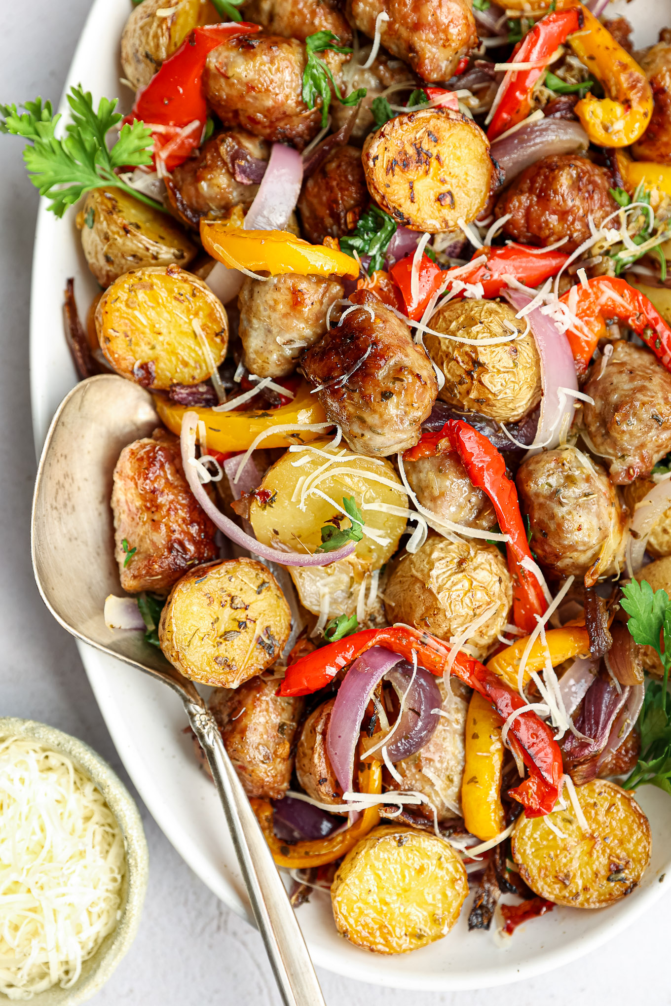 close up roasted sausage with potatoes with a side of serving spoon on the side.