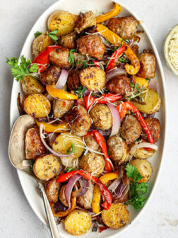 roasted italian sausage, onions, peppers, and potatoes on a white platter garnished with parsley.