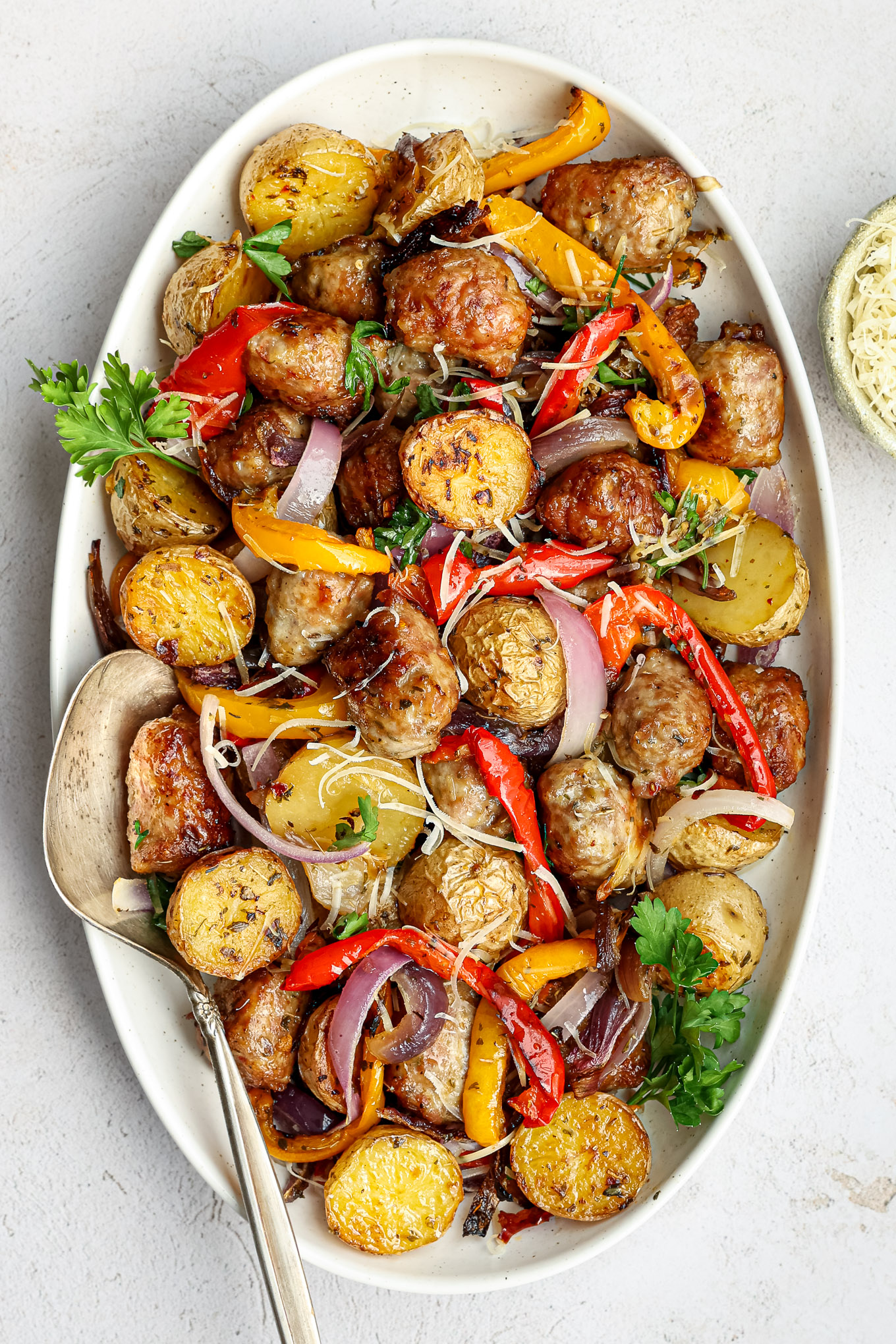 roasted italian sausage, onions, peppers, and potatoes on a white platter garnished with parsley.