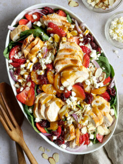 chicken salad with strawberries and spinach in a white bowl.