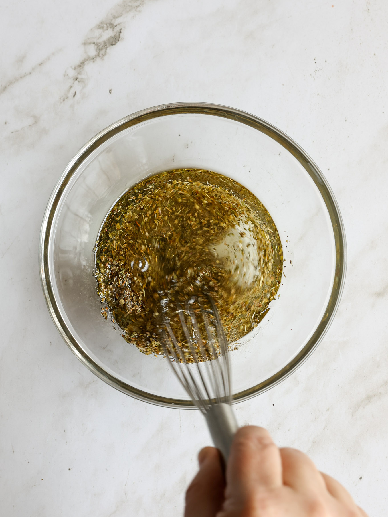oil with spices in a glass bowl being whisked.