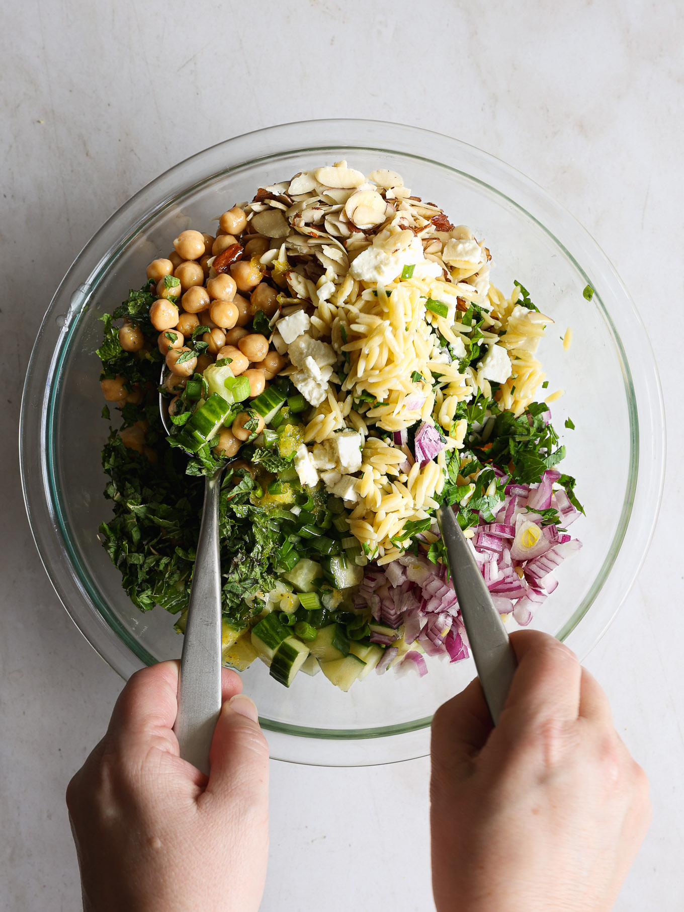 orzo salad being tossed with two spoons.