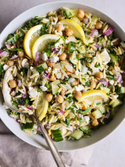 orzo salad recipe in a white bowl garnished with lemons.