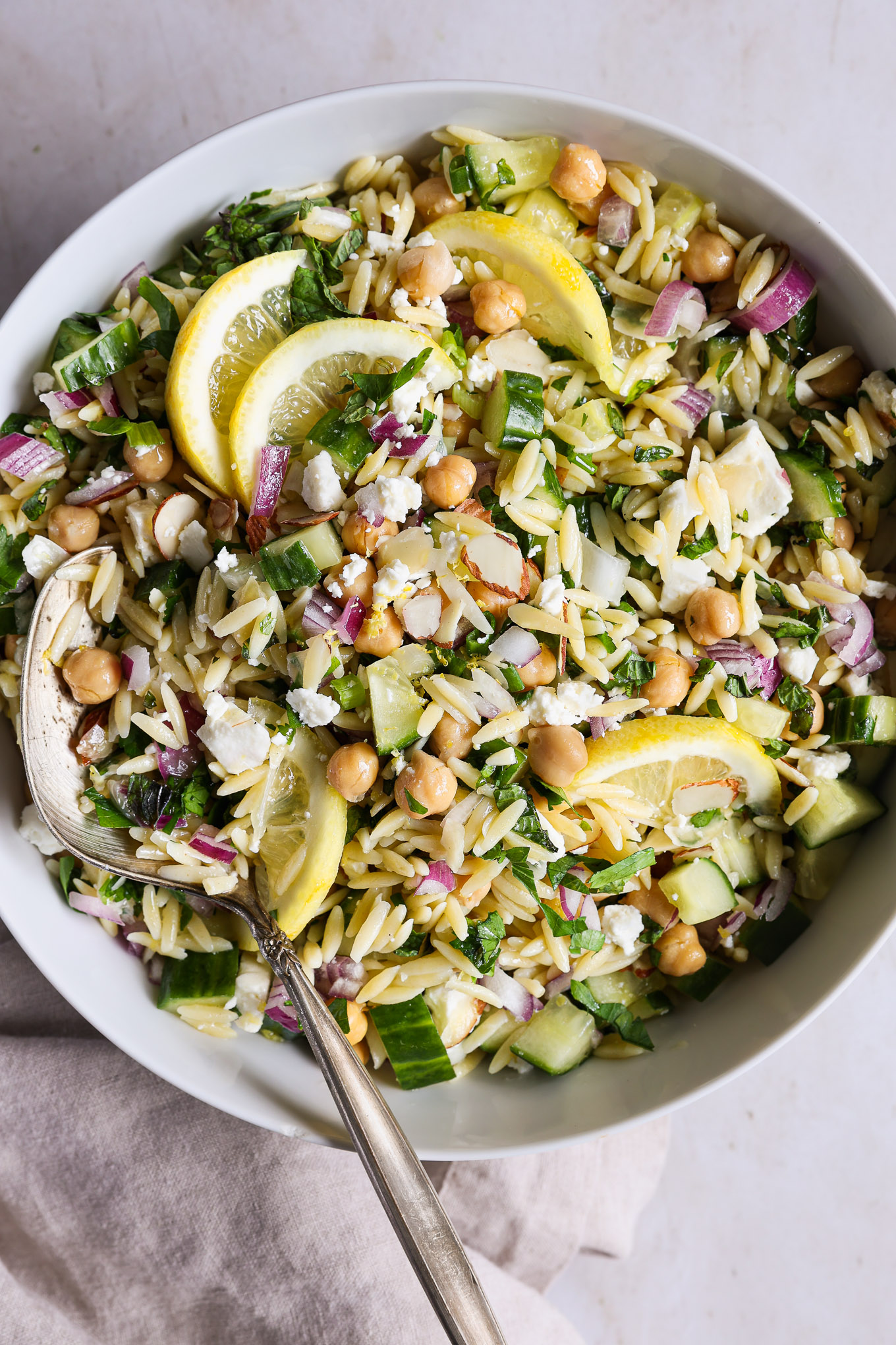 orzo salad recipe in a white bowl garnished with lemons.