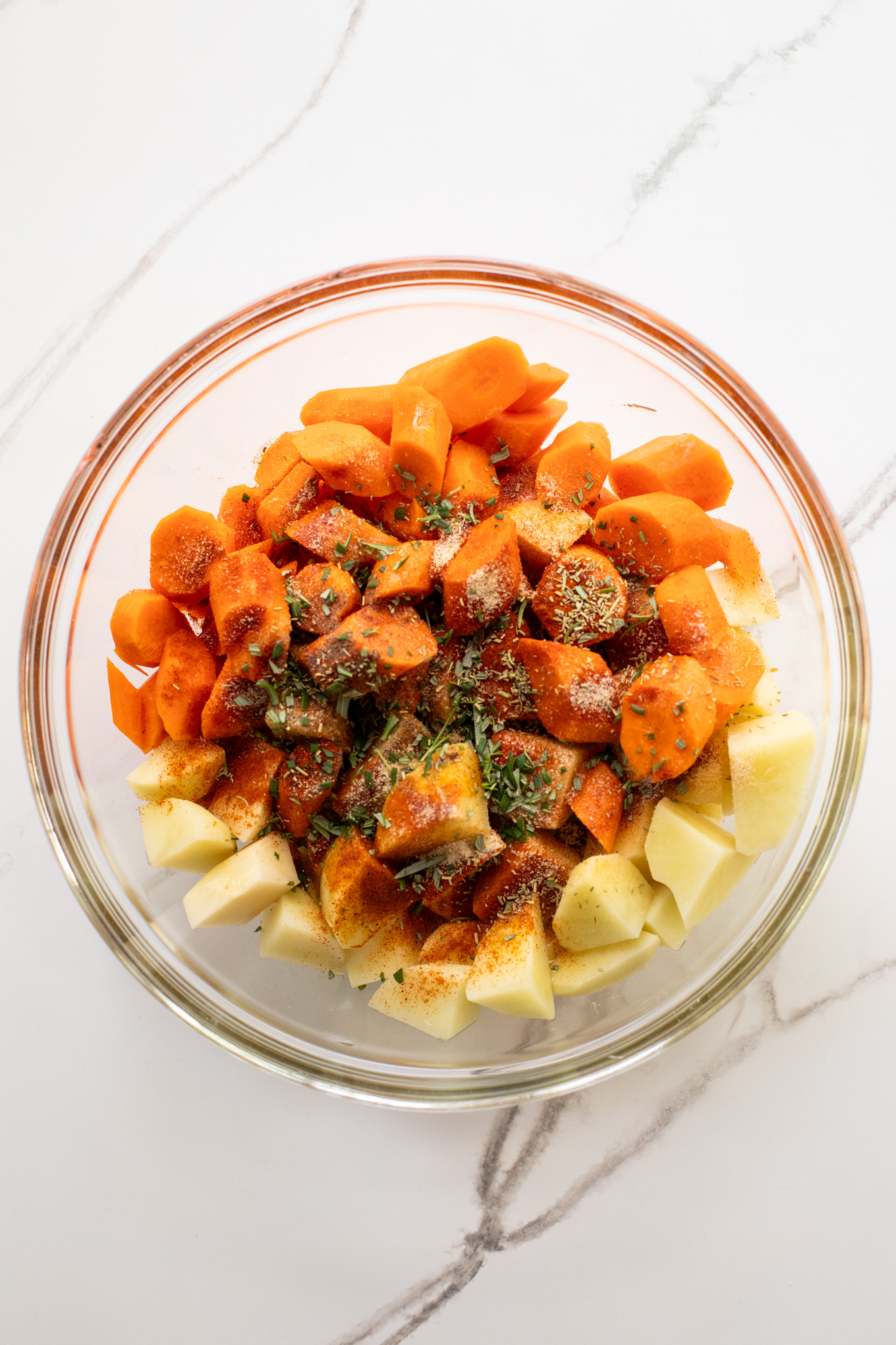 cut up carrots and potatoes in a glass bowl with oil and spices.