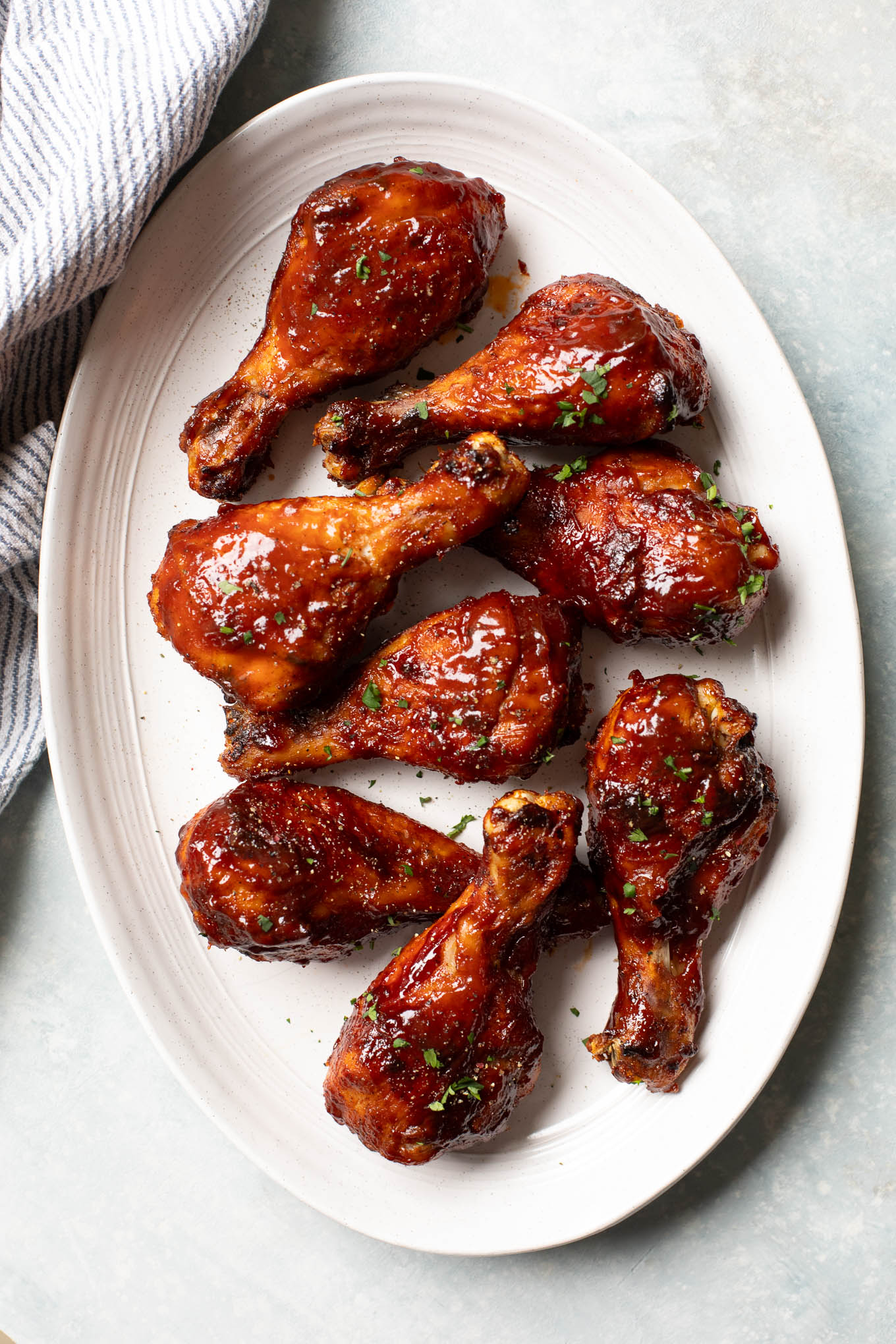 roasted chicken legs on an oval platter topped with BBQ sauce.
