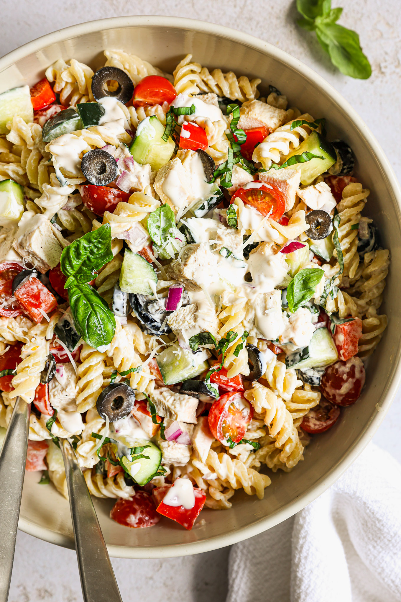 chicken pasta salad in a white bowl garnished wiht basil.