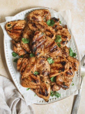 grilled chicken thighs on a platter garnished with cilantro.