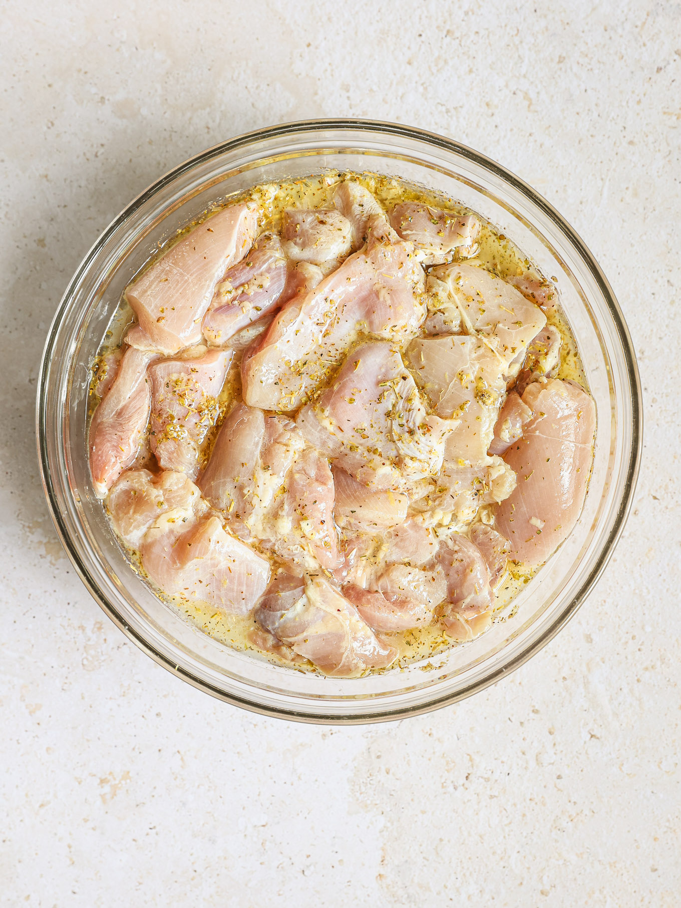 chicken thigh chunks mixed with lemon marinade in a glass bowl.