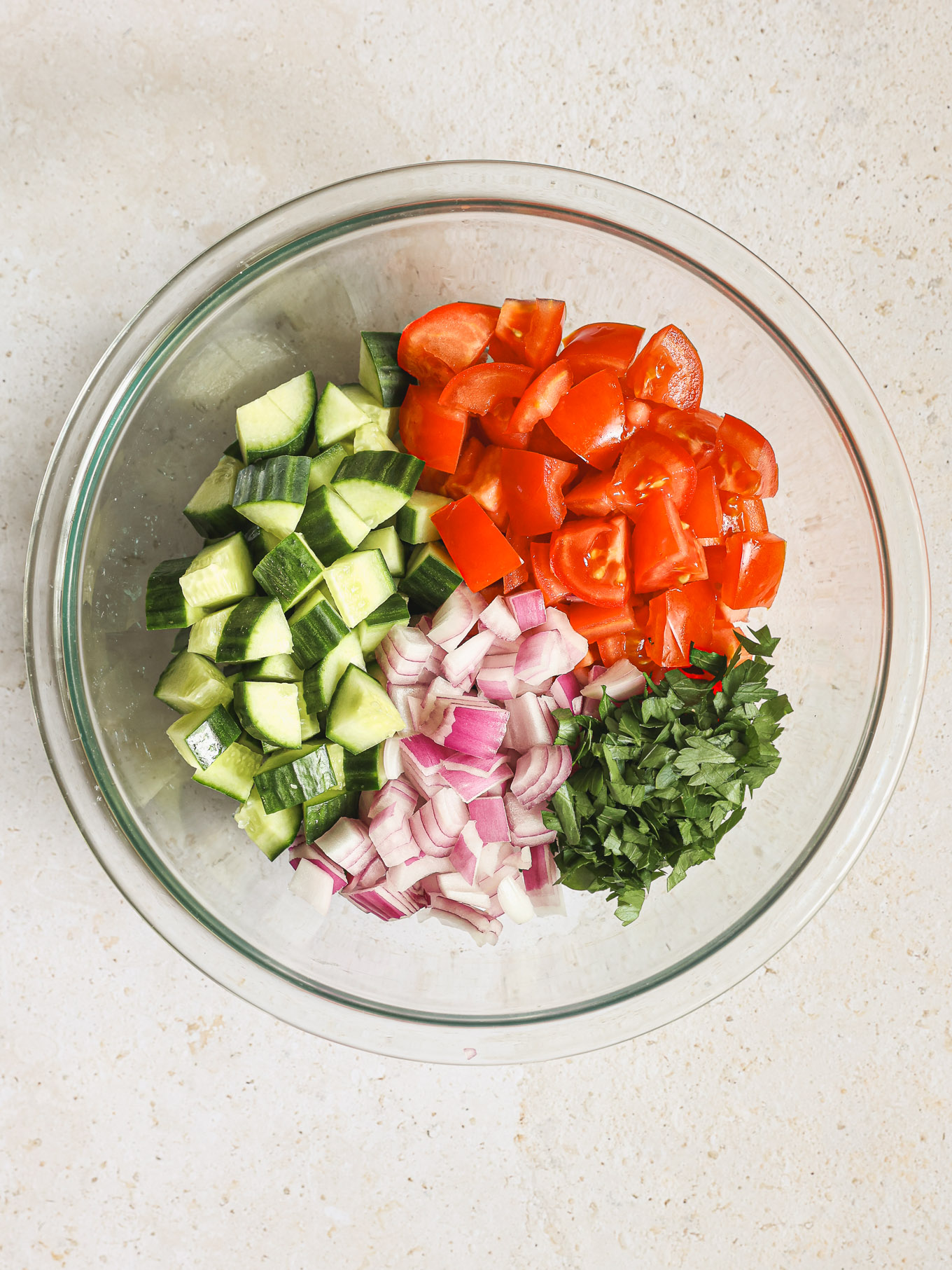 cut up tomatoes, cucumbers, onions, and parsley in a bowl.
