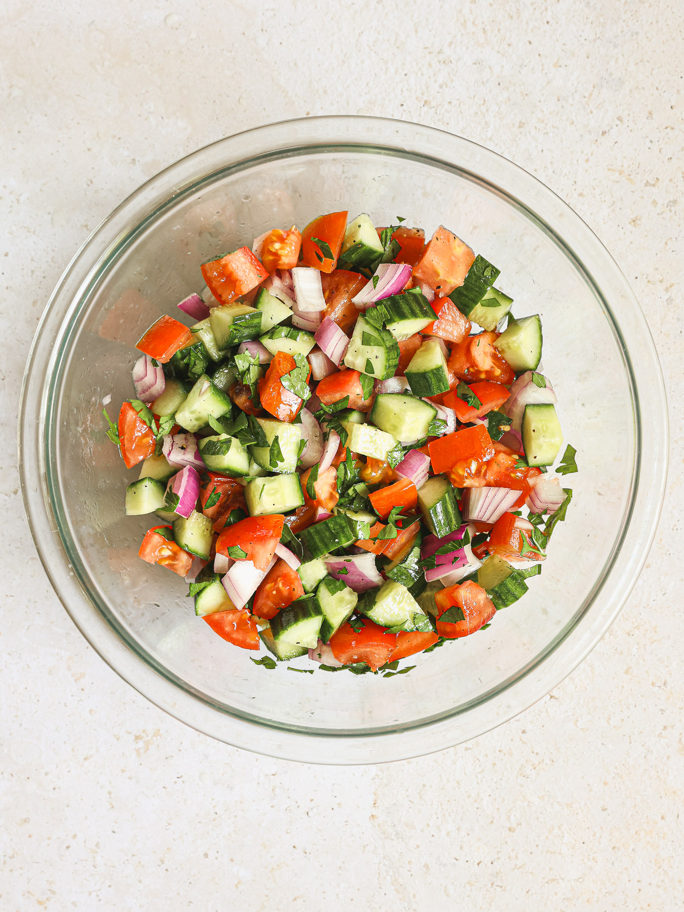 tosses cucumber tomato salad in a glass bowl.