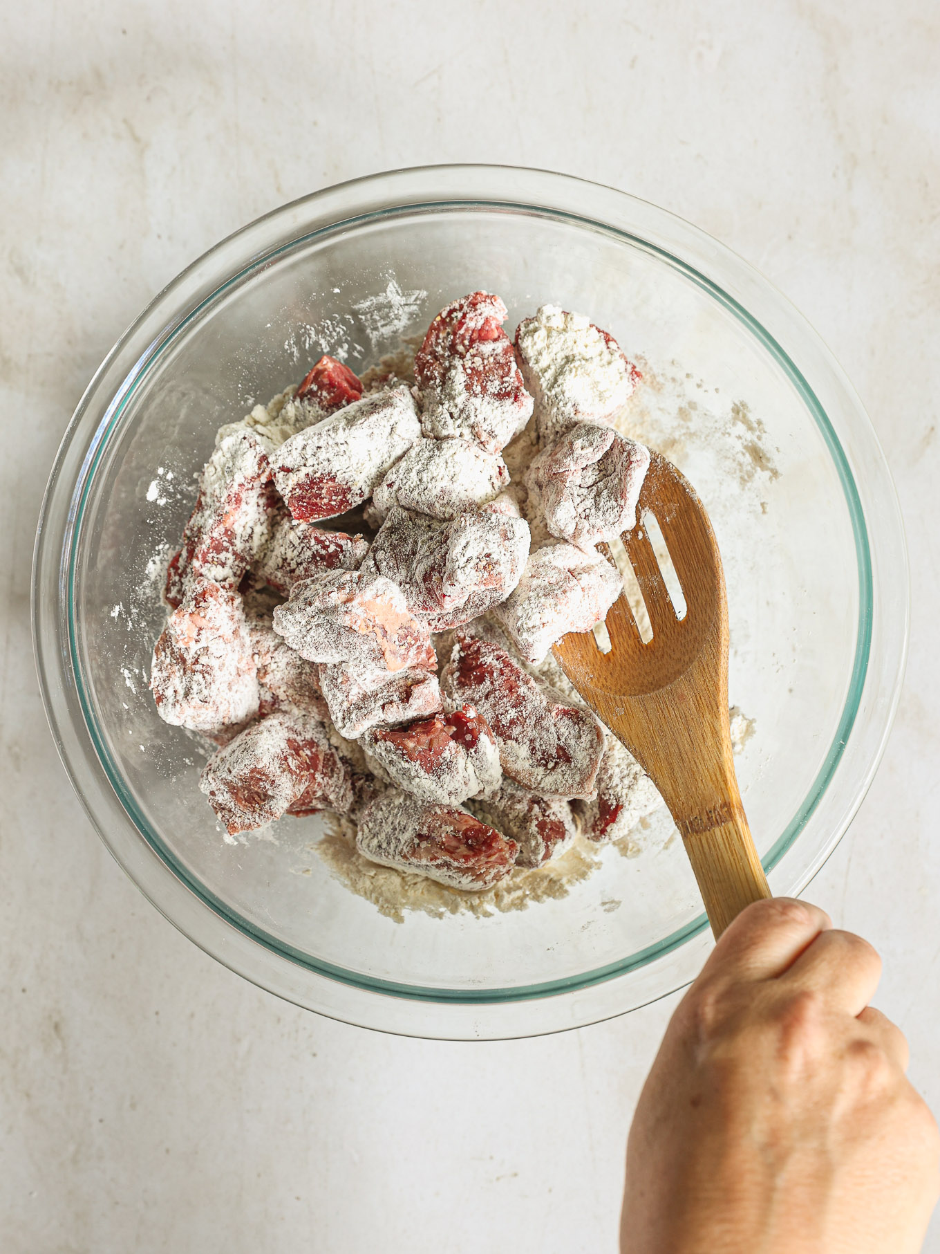 beef cubes in a glass bowl tossed with flour.