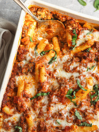 ziti pasta with meat and cheese in white baking dish with a spoon.
