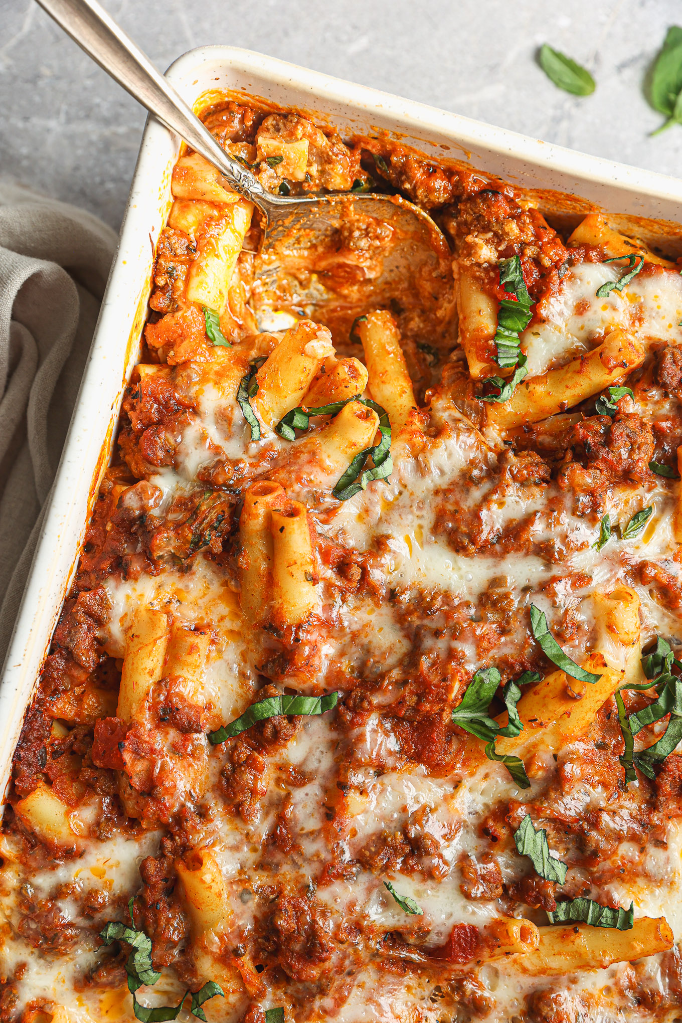 ziti pasta with meat and cheese in white baking dish with a spoon.