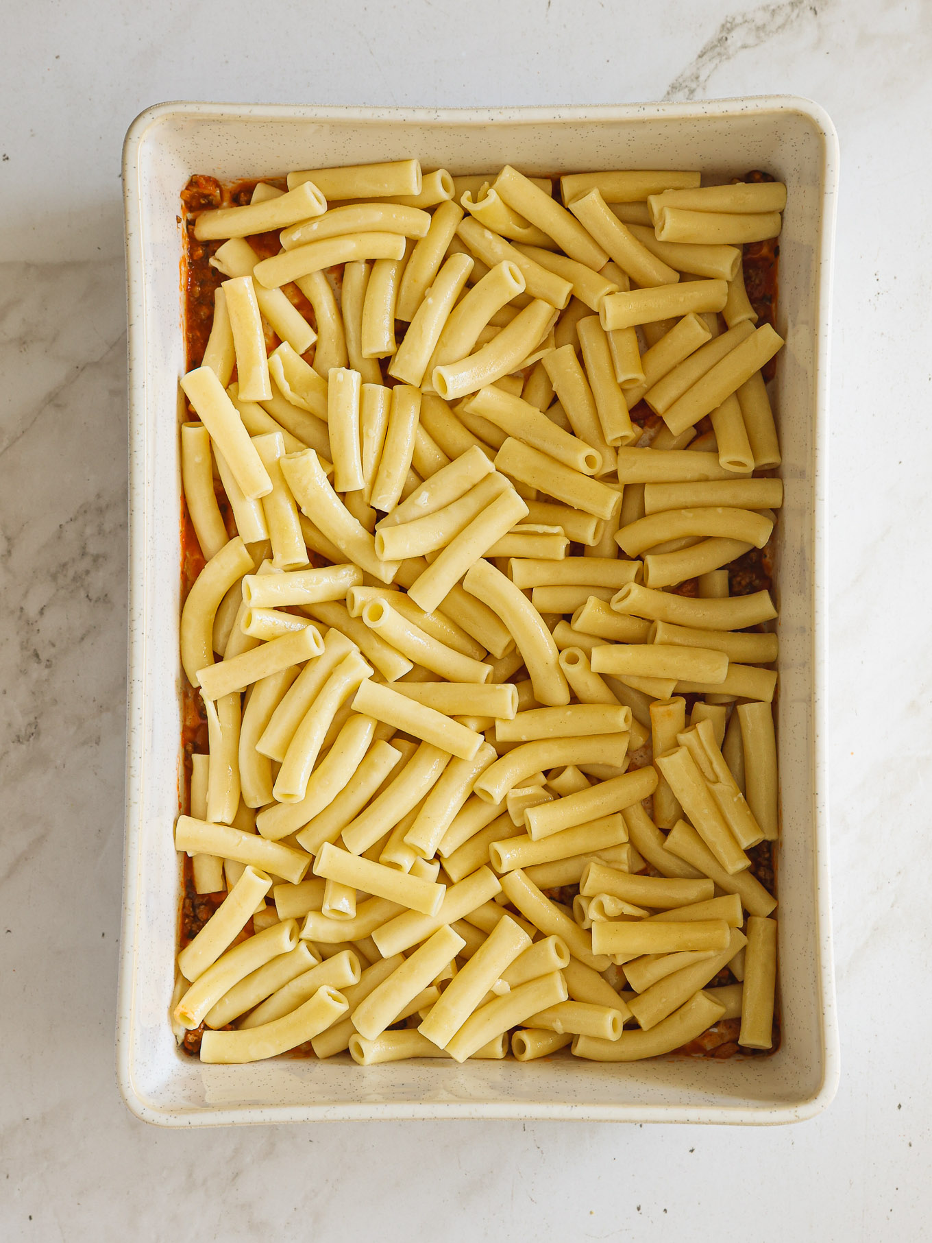 layered ziti pasta with sauce in a baking dish.